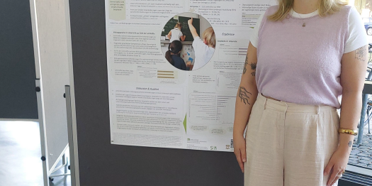 Das Foto zeigt Pauline Schröder, die in einem hellen Veranstaltungsgebäude neben einer großen Posterwand steht und in die Kamera lächelt. Auf der Posterwand befindet sich ihr wissenschaftliches Poster mit dem Titel „Bildungssprachlich handeln im Unterrichtsdiskurs – Eine Befragung von Lehrkräften zu Bildungssprache und Fachgesprächen im Unterricht“. Das Poster enthält verschiedene Textabschnitte, Grafiken und Abbildungen und ist als Beitrag „10a“ gekennzeichnet.