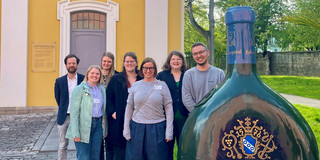 Das AuThenTo-Projektteam mit Verantwortlichen anderer Projekte der GamKi-Förderlinie Sieben Menschen stehen nebeneinander vor einem Gebäude. Sie gucken alle in die Kamera.